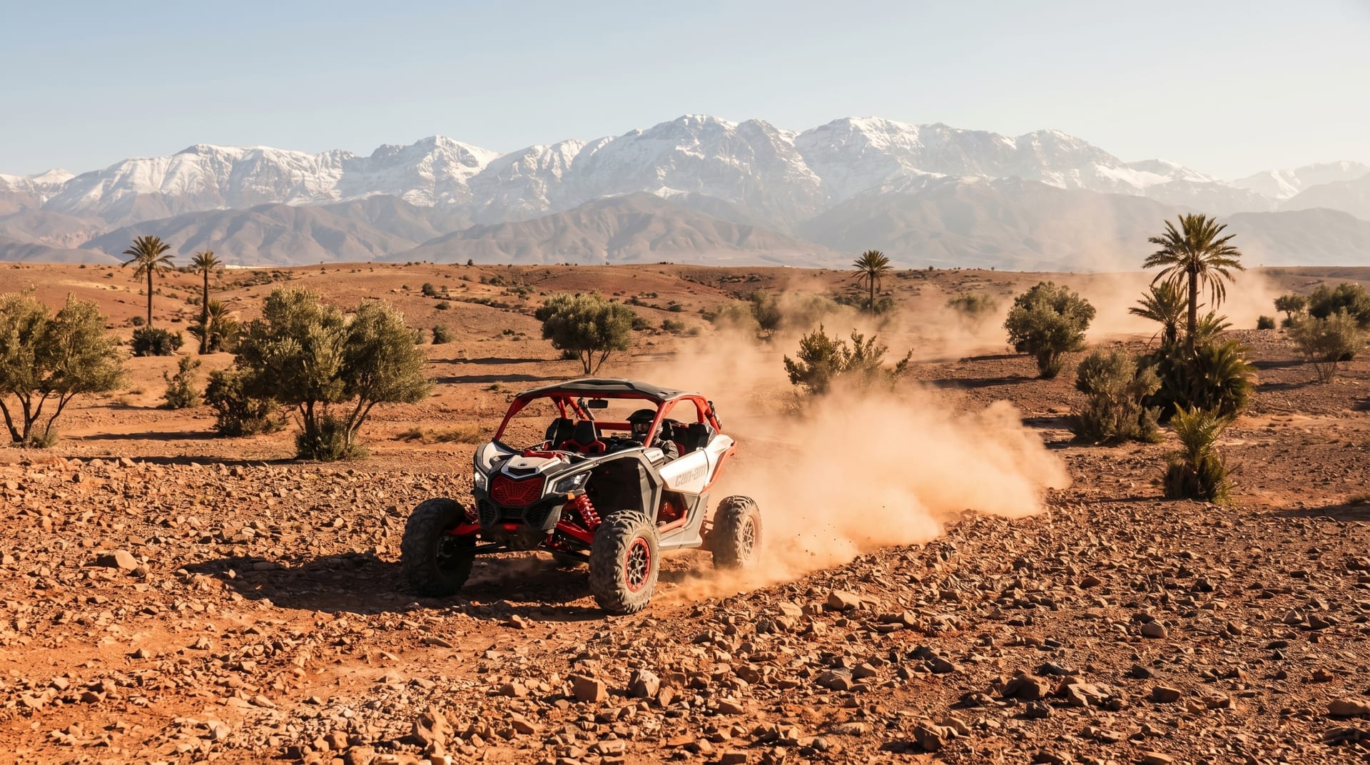 Buggy Can-Am soulevant la poussière entre les palmiers, Haut Atlas enneigé au fond
