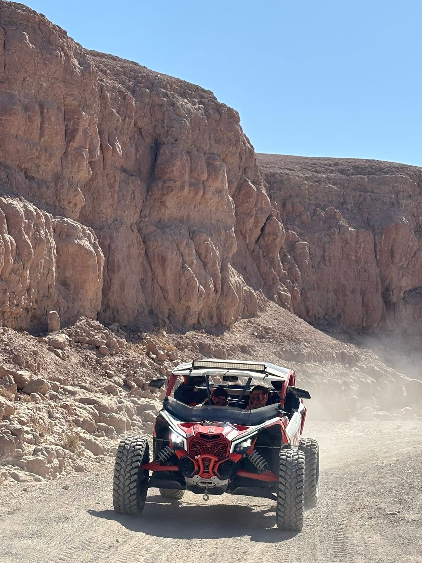 Buggy Can-Am rouge et blanc sur une piste au pied d’une falaise ocre