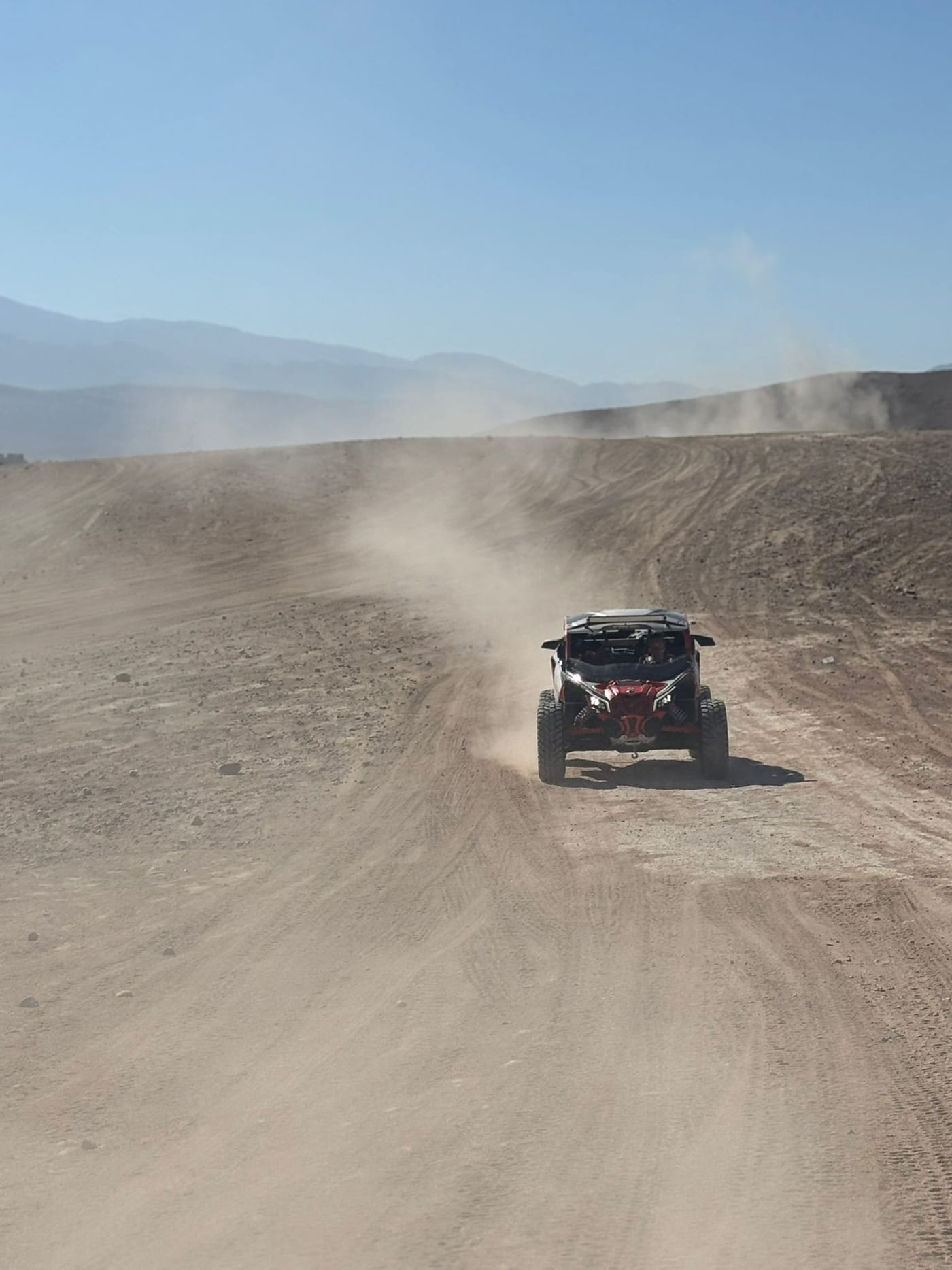 Buggy rouge sur une large piste poussiéreuse, collines voilées de poussière au fond
