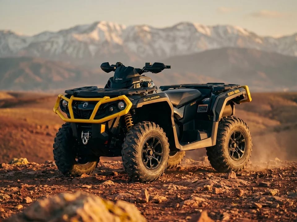Quad Can-Am Outlander à l’arrêt sur un sol rocailleux, chaîne enneigée à l’horizon