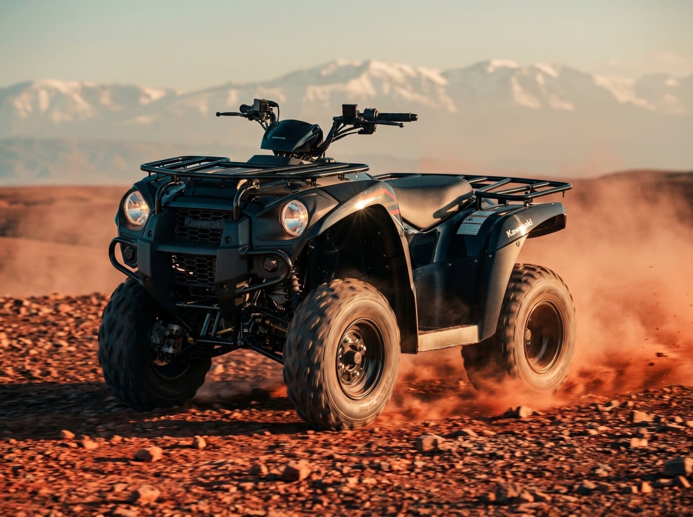 Quad Kawasaki Brute Force 300 en action sur une piste rocheuse d’Agafay, Atlas enneigé au fond